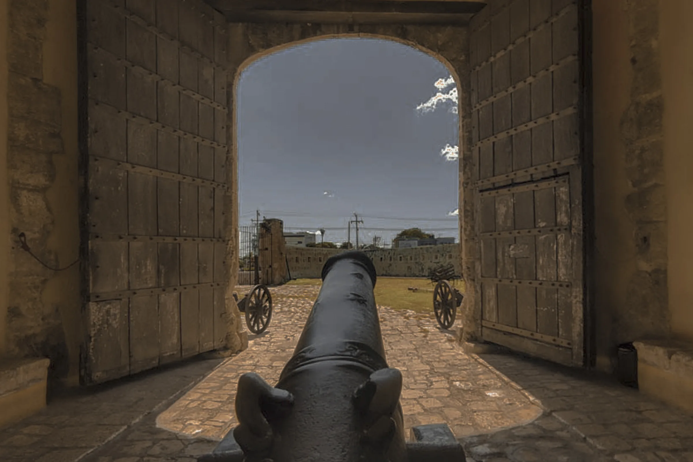Cañón frente al arco abierto de la Puerta de Tierra, en la muralla de Campeche, con sus portones de madera