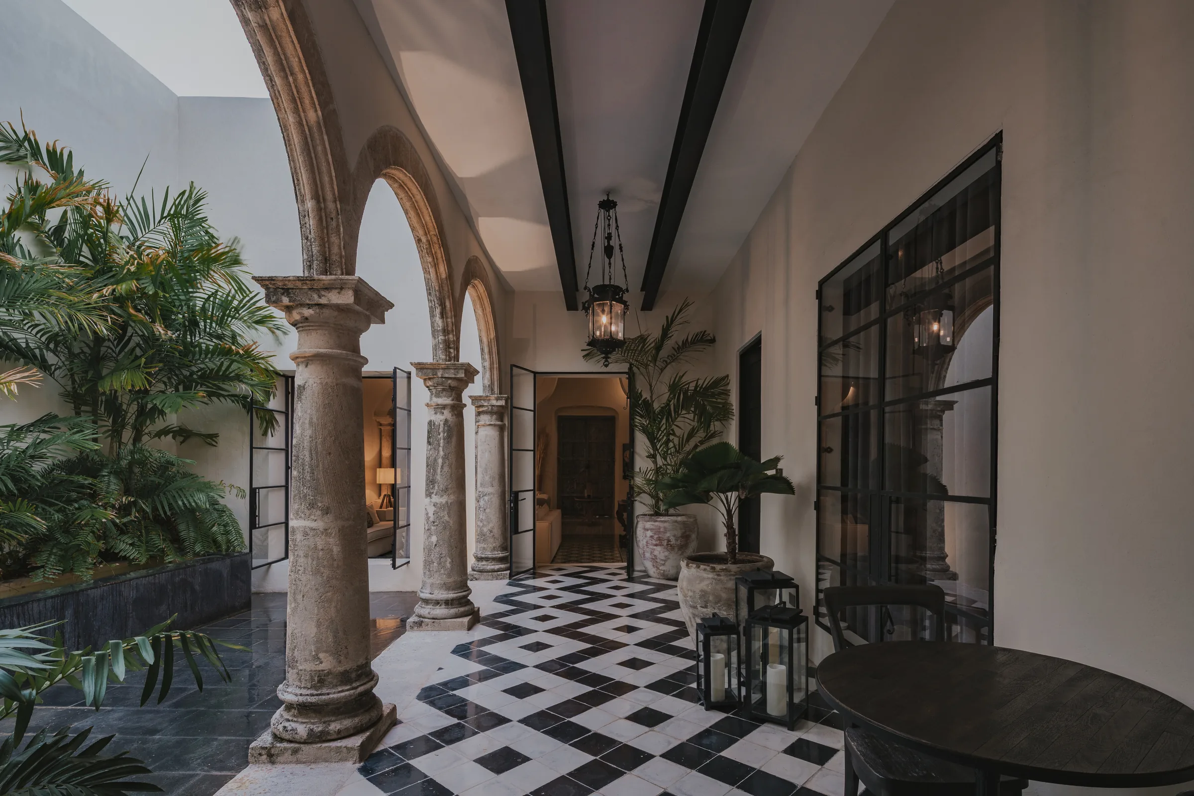 Arcada del patio central de Casa Japa, con columnas de piedra, piso de pasta en damero y faroles