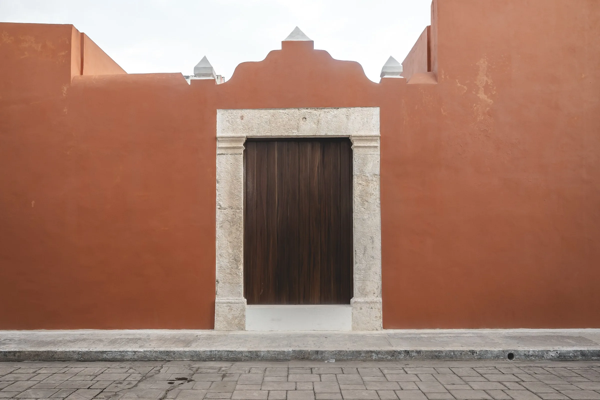 Fachada terracota de Casa Ex-Templo con remate mixtilíneo y portón de madera, en Campeche