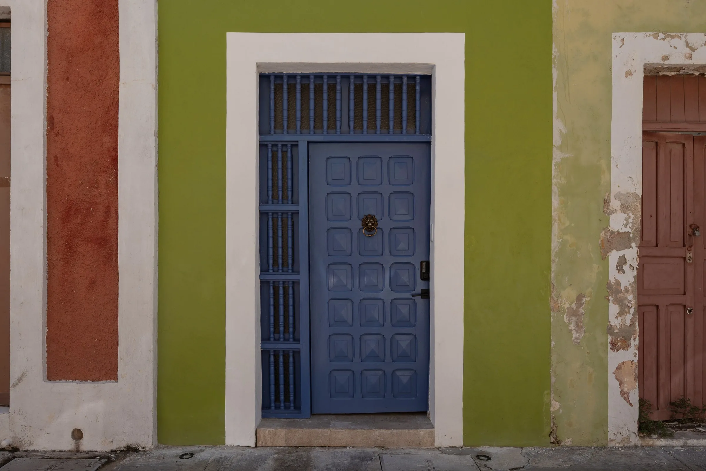 Puerta azul con marco blanco en la fachada verde de Casa Pistache, en Campeche