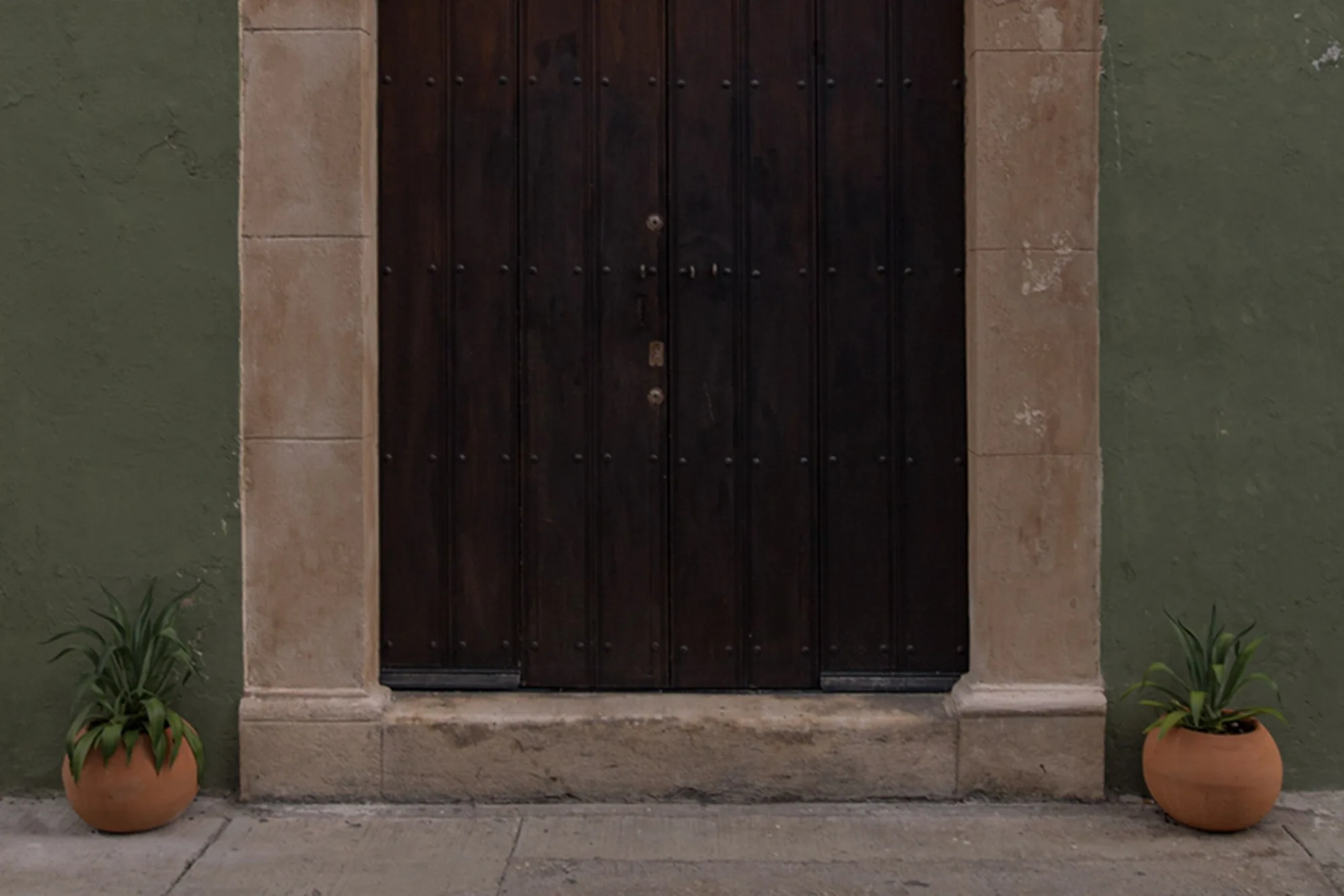 Portón de madera oscura con marco de piedra y macetas a los lados, en la casona de Narrativ Lofts de la Calle 12