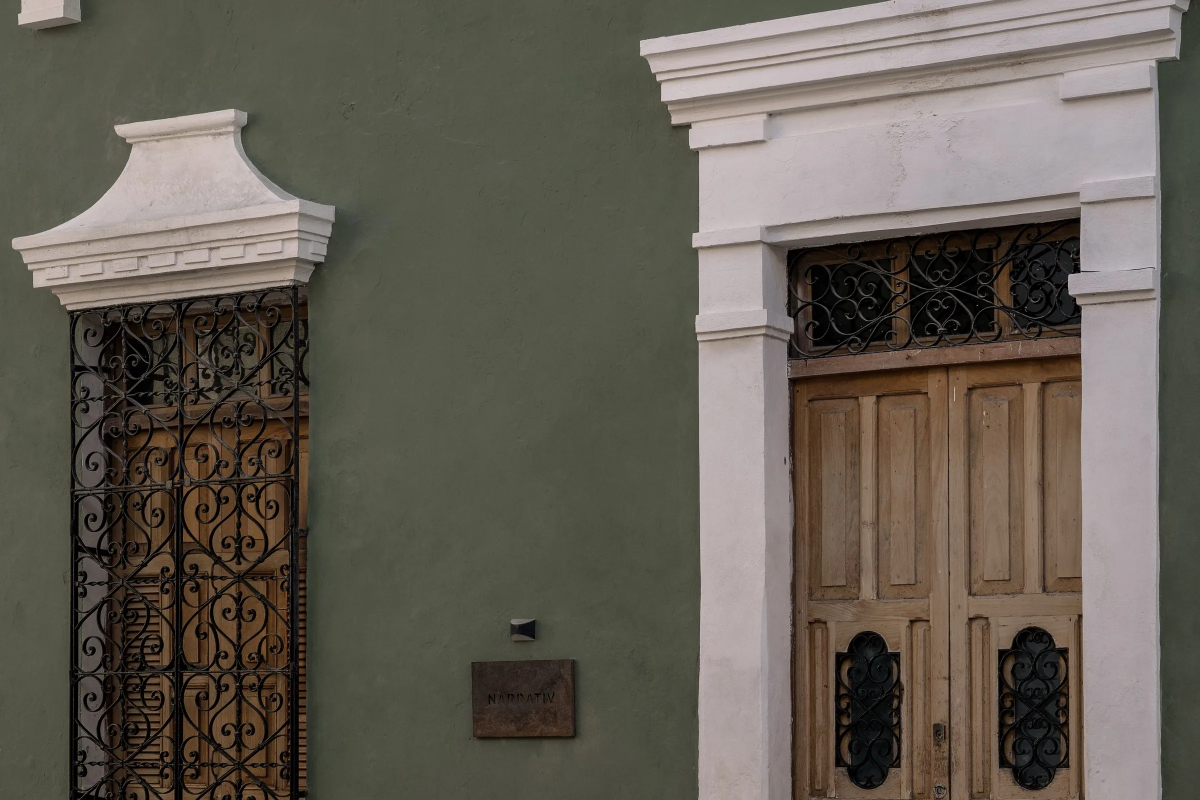 Puerta de herrería y puerta de madera en la fachada verde de la casona de Narrativ Lofts en la Calle 59 de Campeche