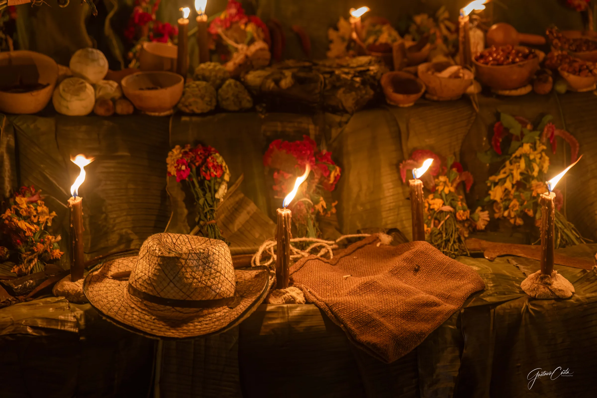 Altar de Hanal Pixán con velas encendidas, flores, jícaras y un sombrero de palma