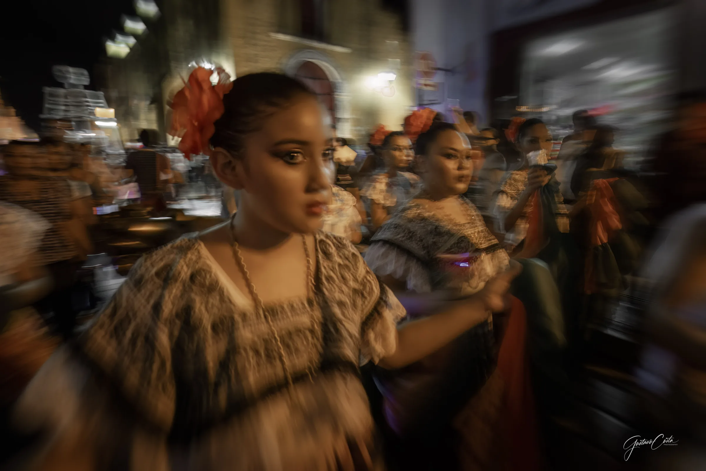 Bailarinas con traje regional y flores en el cabello recorren de noche una calle del centro histórico de Campeche
