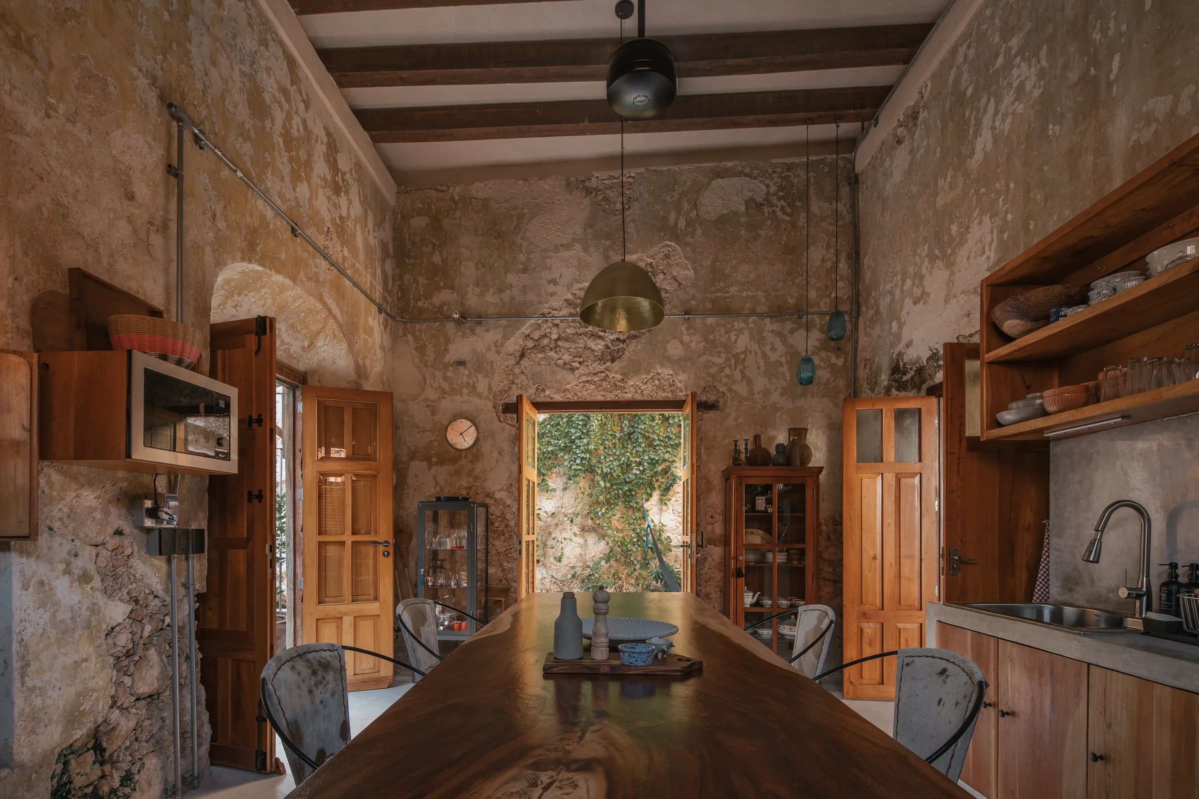 Cocina y comedor de Casa Zotz con una mesa larga de madera, muros de piedra a la vista y puertas abiertas a un patio con enredadera
