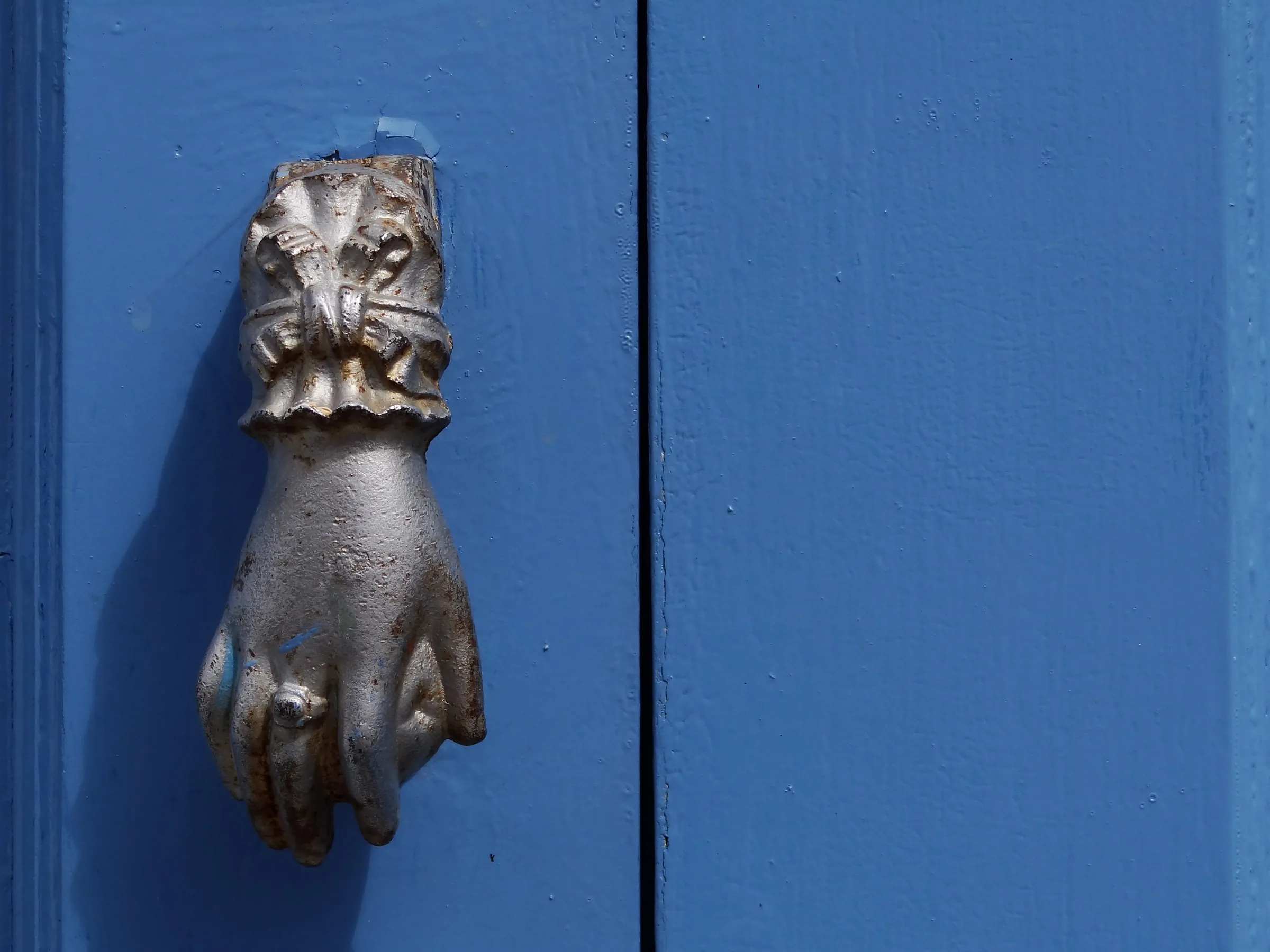 Aldaba de hierro en forma de mano sobre una puerta de madera pintada de azul en el centro histórico de Campeche
