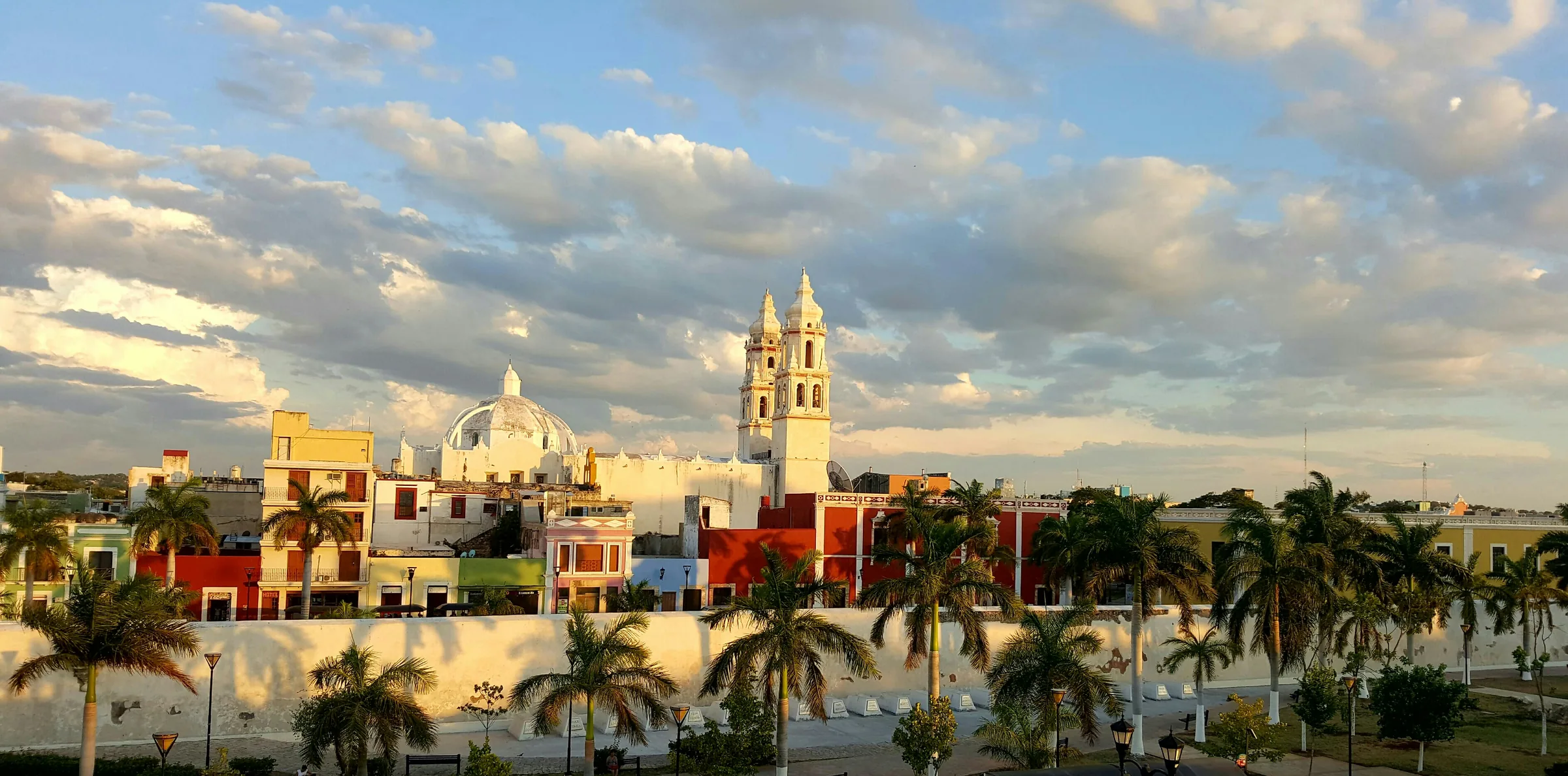 Vista del centro histórico de Campeche con las torres de la Catedral, una cúpula y casas de colores detrás de una hilera de palmeras
