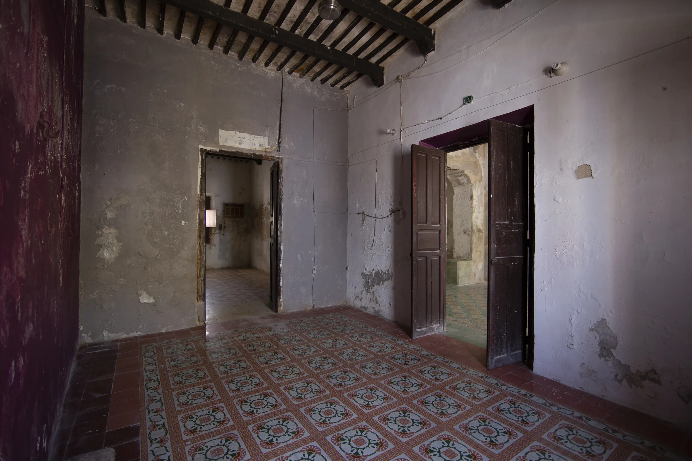 Habitación de La Casa Verde antes de la restauración, con techo de vigas, piso de pasta y puertas de madera