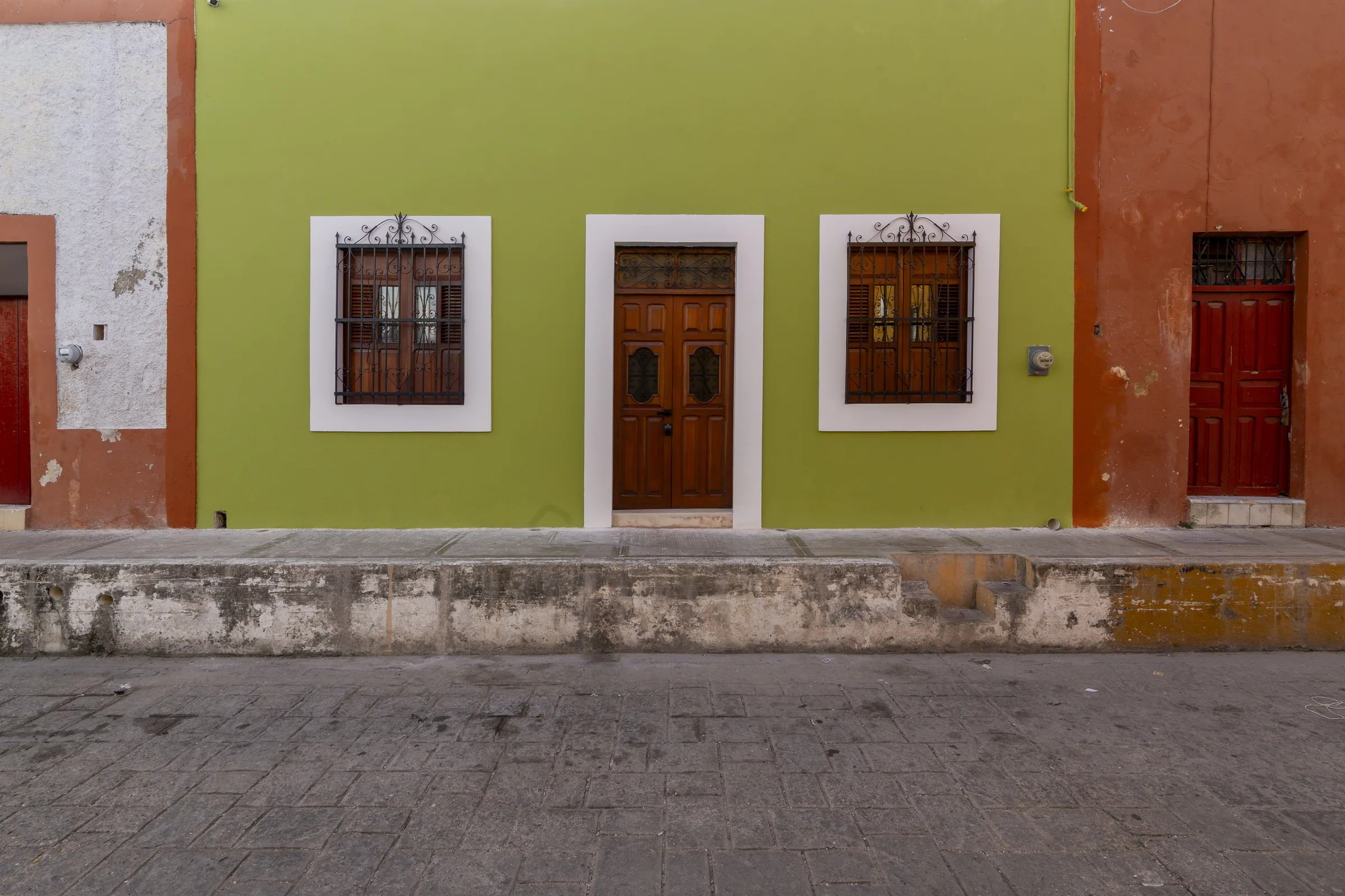 Fachada verde restaurada de La Casa Verde, con puerta y ventanas de madera, en una calle de la ciudad amurallada de Campeche