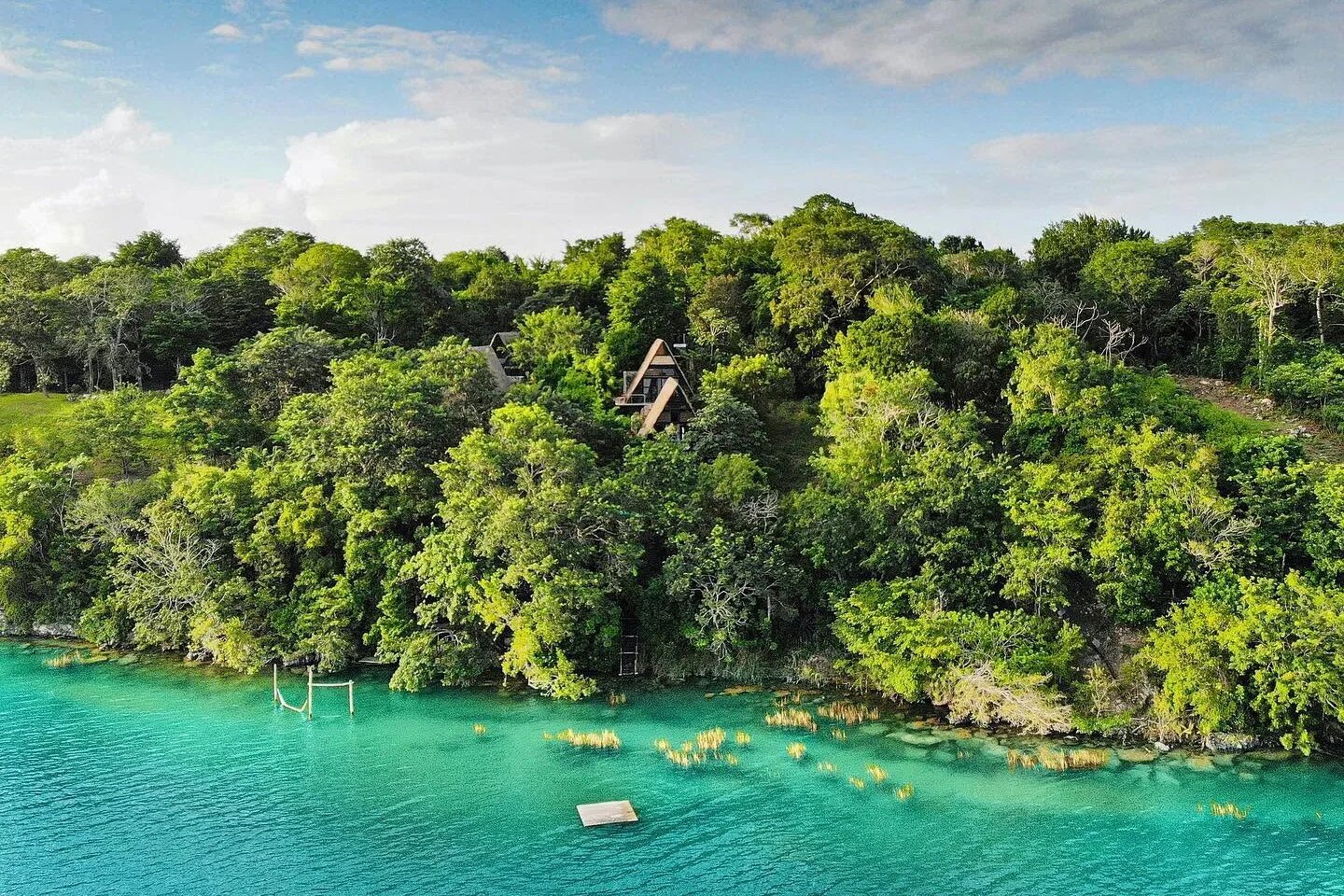 Vista aérea de las cabañas en forma de A de Azul Nomeolvides entre la selva, sobre la orilla turquesa de la laguna de Bacalar