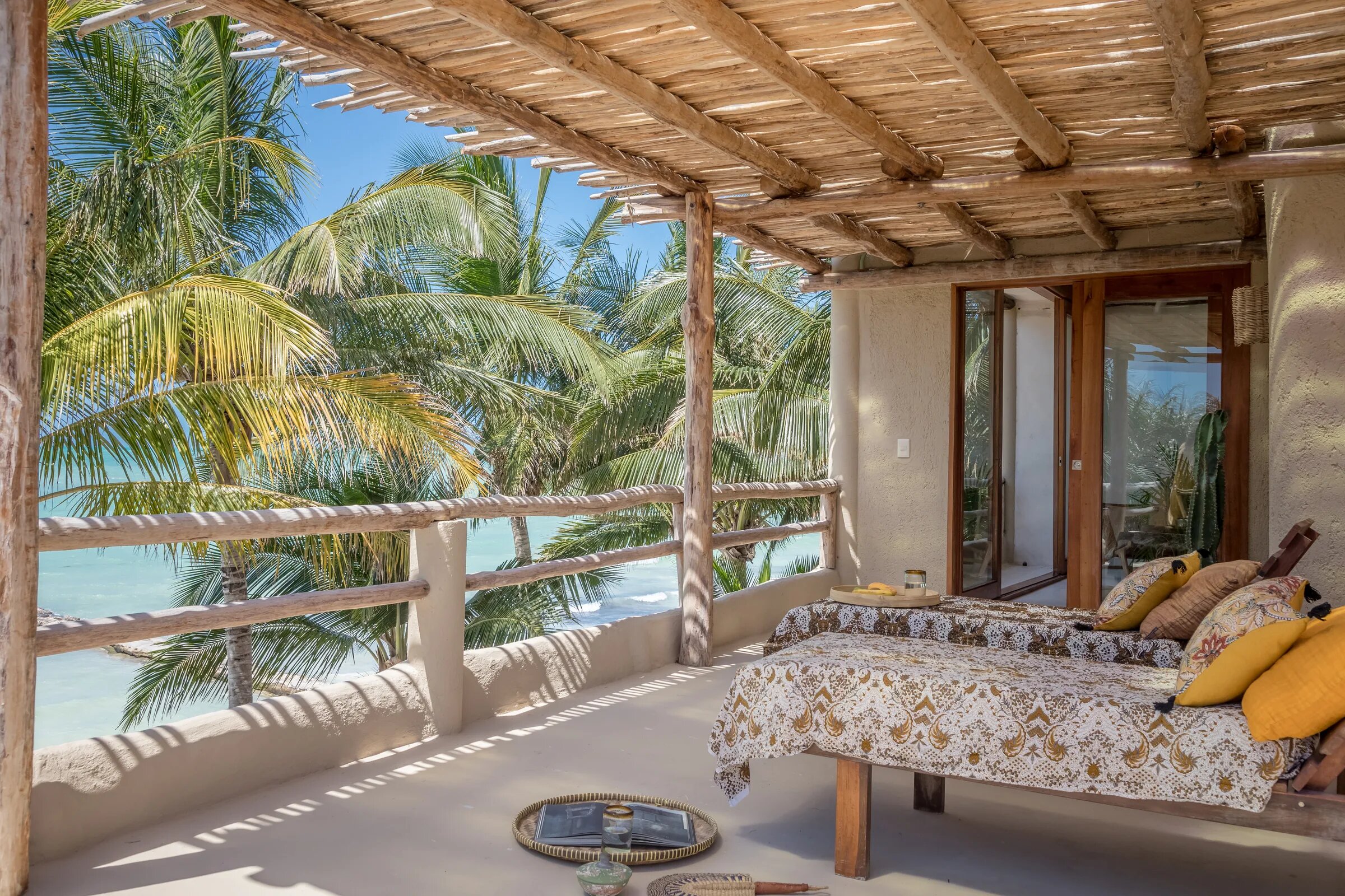 Terraza techada de Casa Cat Ba con dos camastros y cojines amarillos, entre palmeras y frente al mar de Holbox